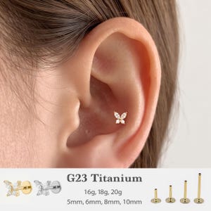May include: A gold-tone butterfly-shaped ear stud featuring four marquise-cut clear stones. The jewelry is made of G23 titanium and is available in 16g, 18g, and 20g gauges with post lengths of 5mm, 6mm, 8mm, and 10mm as shown in the image.