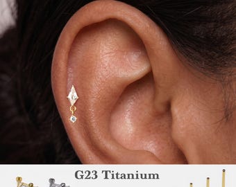Könnte beinhalten: Ein goldfarbener Knorpel-Ohrstecker aus G23-Titan mit einem drachenförmigen, klaren Schmuckstein und einem kleinen, hängenden runden Stein. Der Text G23 Titanium, 16g, 18g, 20g sowie 5mm, 6mm, 8mm, 10mm ist neben verschiedenen Stablängen abgebildet.
