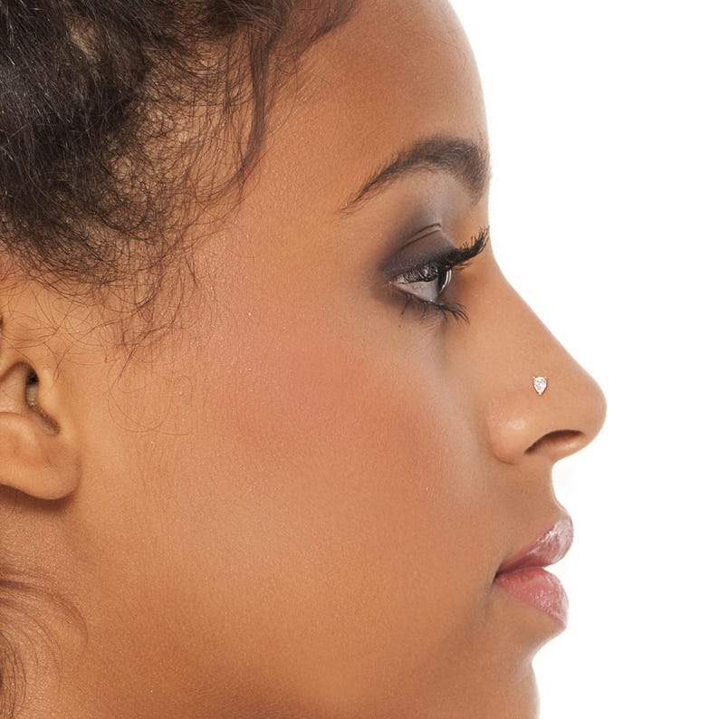 K&ouml;nnte beinhalten: Nahaufnahme eines Gesichts, das einen kleinen, klaren Nasenring in Herzform zeigt.