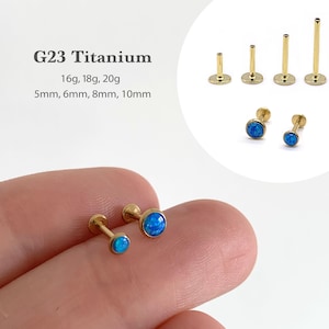 May include: Gold-colored G23 titanium earrings with blue opal stones. The image shows various sizes, including 16g, 18g, and 20g, with lengths of 5mm, 6mm, 8mm, and 10mm. The text "G23 Titanium" is also visible.