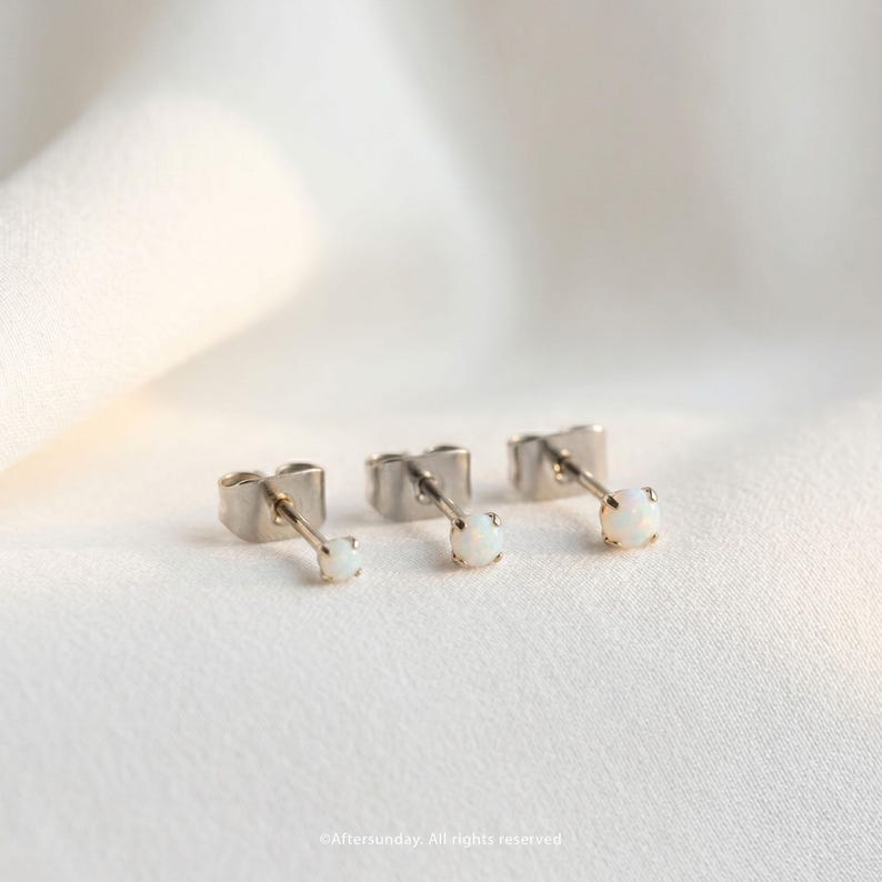 Peut inclure: Trois boucles d'oreilles &agrave; tige de couleur argent&eacute;e, chacune dot&eacute;e d'une petite pierre ronde blanche iris&eacute;e fix&eacute;e dans un serti &agrave; quatre griffes. Les boucles d'oreilles sont align&eacute;es, montrant le m&eacute;canisme de tige et de fermoir papillon.
