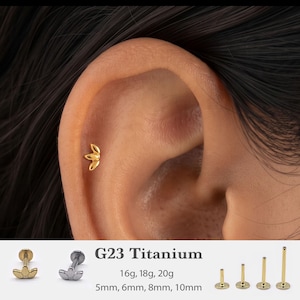 May include: A gold-colored ear stud with a three-petal leaf design. The product is G23 titanium, available in 16g, 18g, and 20g gauges, with post lengths of 5mm, 6mm, 8mm, and 10mm. The stud is shown inserted into the cartilage of an ear.