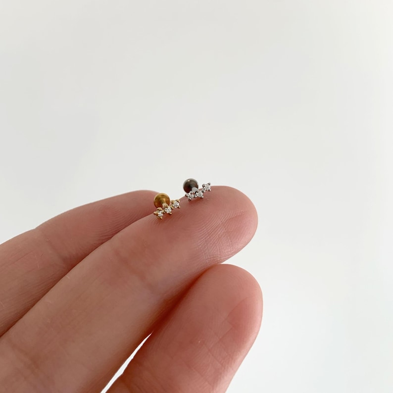 Pu&ograve; includere: Due orecchini a lobo con retro piatto, uno color oro e uno color argento, ciascuno caratterizzato da un design a barra orizzontale con tre piccole pietre chiare incastonate. Gli orecchini hanno una chiusura circolare e una struttura sottile.