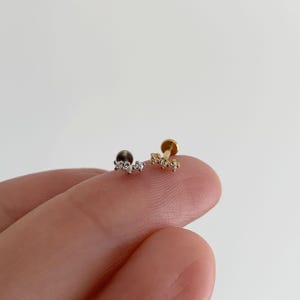 Pu&ograve; includere: Due orecchini a lobo con retro piatto caratterizzati da un design a barra curva con tre piccole pietre trasparenti. Un orecchino &egrave; color argento e l'altro color oro. Ogni orecchino ha una base circolare e una parte superiore decorativa.