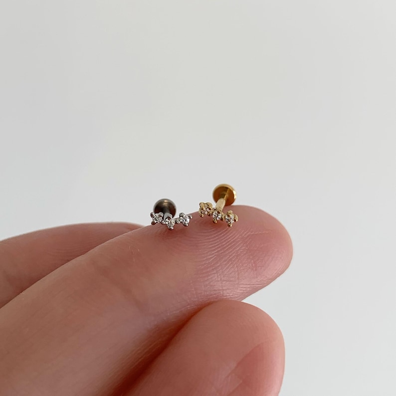 Pu&ograve; includere: Due orecchini a lobo con retro piatto caratterizzati da un design a barra curva con tre piccole pietre trasparenti. Un orecchino &egrave; color argento e l'altro color oro. Ogni orecchino ha una base circolare e una parte superiore decorativa.