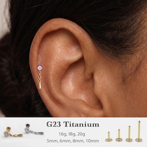 May include: A gold-tone cartilage earring featuring a small clear gemstone stud connected to a short chain with a teardrop charm. The text G23 Titanium, 16g, 18g, 20g, and 5mm, 6mm, 8mm, 10mm is visible alongside four flat-back posts of varying lengths.