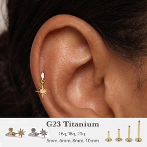 Könnte beinhalten: Ein goldfarbener Stern-Ohrhänger mit einem kleinen klaren Stein, eingesetzt in ein Ohrpiercing. Der Text G23 Titanium, 16g, 18g, 20g sowie 5mm, 6mm, 8mm, 10mm ist zusammen mit Bildern des Schmuckstücks und verschiedenen Stablängen abgebildet.