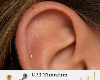 May include: A close-up of a person's ear with a small gold stud earring. The earring is a teardrop shape and is made of G23 titanium. The image also shows different sizes of the earring, ranging from 5mm to 10mm, and gauges of 16g, 18g, and 20g.
