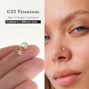 May include: Gold-colored nose rings with a flower design, featuring small, clear gemstones. The image shows two nose rings, one in an L shape and the other in a corkscrew shape. The text reads "G23 Titanium 20g/L Shape, Corkscrew Available in 2 different styles."