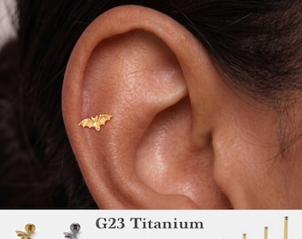 May include: A gold-colored bat-shaped stud earring inserted into an ear cartilage piercing. The image includes text G23 Titanium, gauges 16g, 18g, 20g, and lengths 5mm, 6mm, 8mm, 10mm, alongside views of gold and silver-toned bat studs and flat back posts.