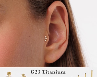 Puede incluir: Joyería de piercing para la oreja de titanio G23 de color dorado con tres piedras preciosas redondas y transparentes. La imagen muestra la joyería en uso en una oreja e incluye variaciones de producto adicionales. El texto en la imagen dice "G23 Titanium" y enumera tamaños.