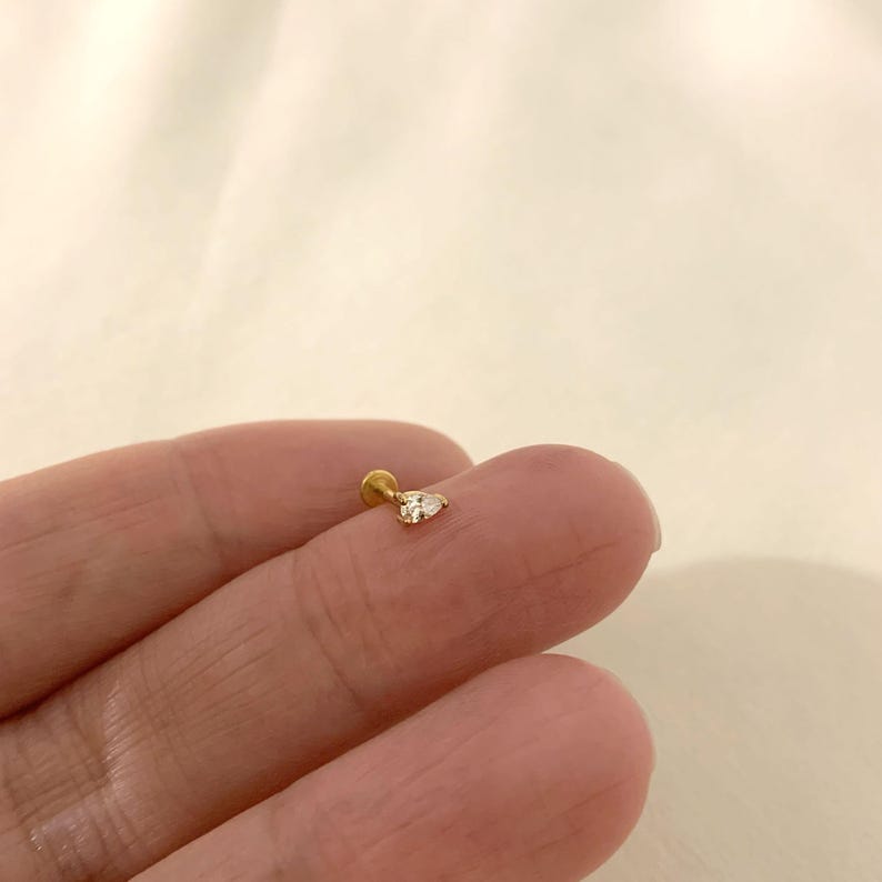 K&ouml;nnte beinhalten: Ein goldfarbener Ohrstecker mit einem klaren birnenf&ouml;rmigen Edelstein.