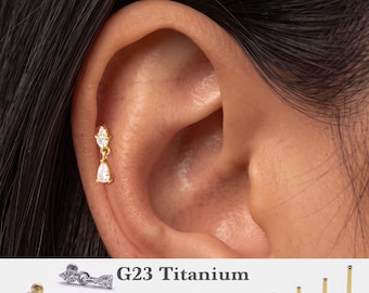 Könnte beinhalten: Ein goldfarbener Ohrstecker mit einem kleinen, klar geschliffenen Marquise-Stein über einem hängenden, birnenförmigen klaren Stein. Der Text G23 Titanium, 16g, 18g, 20g sowie 5mm, 6mm, 8mm, 10mm ist neben dem Schmuckstück und vier Stäben zu sehen.