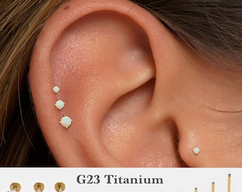 May include: A set of G23 titanium flat back stud earrings featuring white opal stones in varying sizes. The jewelry is available in 16g, 18g, and 20g gauges with post lengths of 5mm, 6mm, 8mm, and 10mm, as shown in the product text and display.