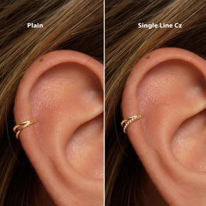 Może przedstawiać: Pokazano dwie złote mankiety na uszy, jedną gładką, a drugą z pojedynczą linią małych, przezroczystych kamieni. Mankiety są noszone na uchu, z tekstem "Plain" i "Single Line Cz" nad każdą mankietą.