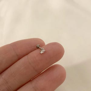 K&ouml;nnte beinhalten: Ein silberner Ohrstecker mit einem klaren, facettierten Edelstein.