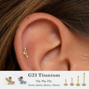 May include: A gold-toned titanium ear piercing with a cluster of yellow and clear gemstones. The earring is shown on an ear, with the text "G23 Titanium" and size options: 16g, 18g, 20g, 5mm, 6mm, 8mm, 10mm.