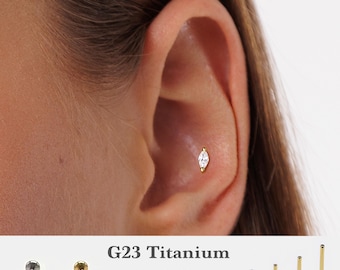 May include: A close-up of a person's ear with a small, clear, marquise-shaped gemstone stud earring. The earring is made of G23 titanium and is available in sizes 5mm, 6mm, 8mm, and 10mm. The text "G23 Titanium" and "16g, 18g, 20g" is visible below the image.