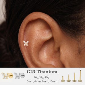 May include: A gold-toned butterfly-shaped stud earring with clear stones, featuring a flat back post. Text displays G23 Titanium, 16g, 18g, 20g, and 5mm, 6mm, 8mm, 10mm, alongside images of gold and silver butterfly studs and four post lengths.