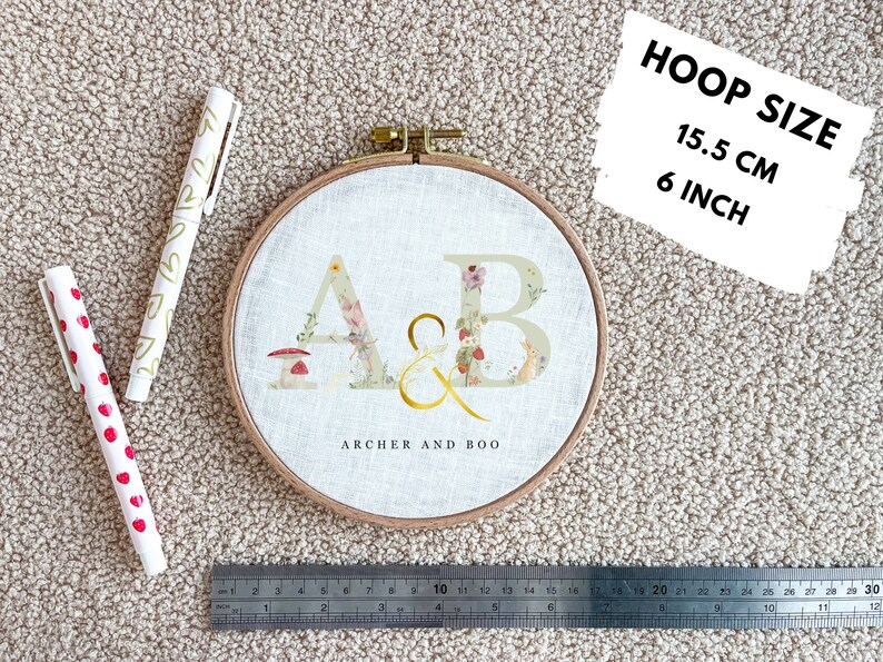 May include: A white embroidery hoop with a floral design and the letters "A & B" in gold. The hoop is 6 inches in diameter and says "Archer and Boo" below the letters.