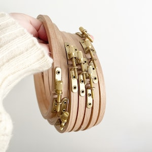 May include: A set of five wooden embroidery hoops with brass tightening knobs. The hoops are nested together and are ready to be used for crafting.