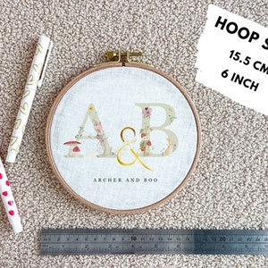 May include: A white embroidery hoop with a floral design and the letters "A&B" in gold. The hoop is 6 inches in diameter and says "Archer and Boo" below the letters.