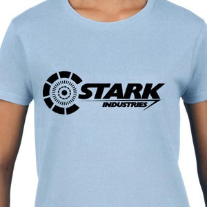 May include: A light blue t-shirt with a black Stark Industries logo. The logo features a stylized circle with a smaller circle inside and the text "Stark Industries" in a bold font.