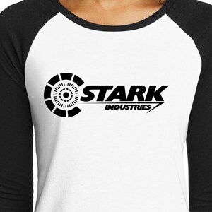 May include: A white and black baseball style t-shirt with a black and white logo that says "Stark Industries" with a circle design in the background.