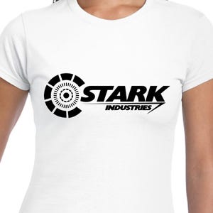 May include: White t-shirt with a black Stark Industries logo. The logo features a circular design with a smaller circle in the center and the text "Stark Industries" in a bold font.