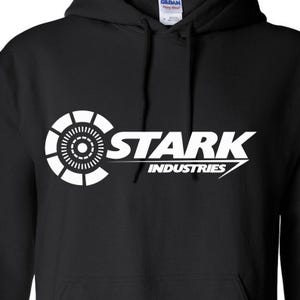 May include: Black hooded sweatshirt with a white graphic of the Stark Industries logo, featuring the Iron Man arc reactor design and the text "Stark Industries".