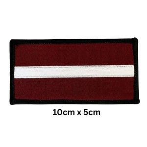 Puede incluir: Parche rectangular con la bandera de Letonia. El diseño presenta un fondo granate con una franja blanca horizontal en el centro. El parche tiene un borde negro y mide 10 cm x 5 cm.