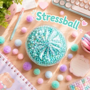Könnte beinhalten: Ein runder, transparenter Stressball gefüllt mit kleinen türkisfarbenen und blauen Perlen, umgeben von bunten Pompons, einem hellblauen Stift, einem Spiralnotizbuch mit Bärenmotiv und einem Notizblock mit dem Text Stressball.