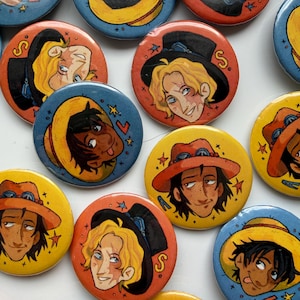 Peut inclure: Une collection de badges ronds illustrés représentant des personnages. Certains badges montrent une personne aux cheveux blonds avec un chapeau noir, tandis que d'autres représentent une personne aux cheveux bruns avec un chapeau de paille jaune.