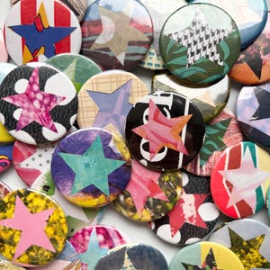 May include: A selection of circular badges with star motifs. The badges display diverse patterns and colours, including pink, blue, green, and yellow. Some stars have patterned backgrounds, while others are solid colours. The badges are closely arranged.