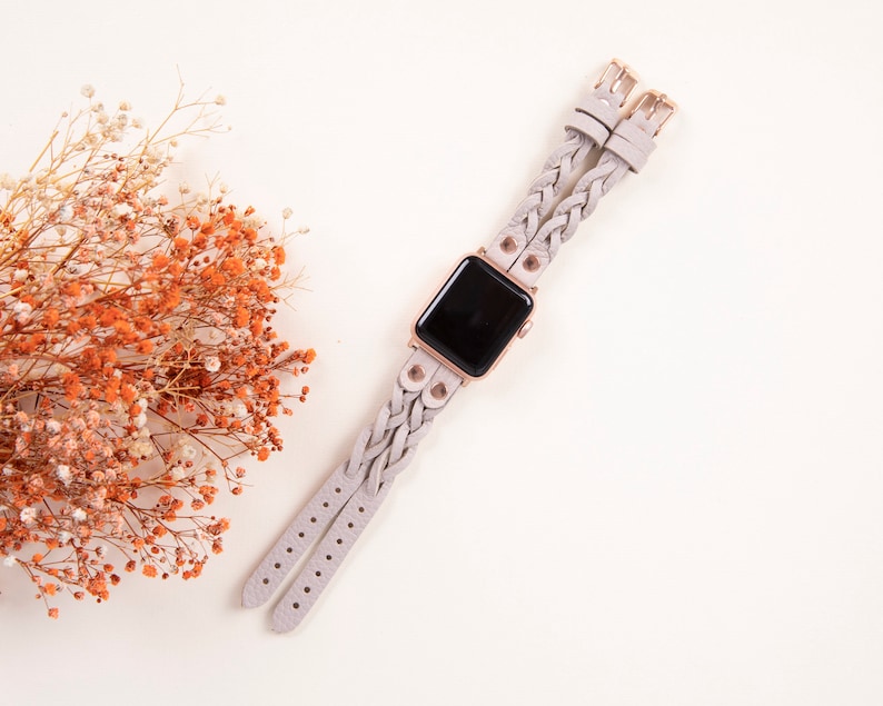 Peut inclure: Un bracelet de montre tress&eacute; gris clair avec des d&eacute;tails en or rose et un cadran noir. Le bracelet est compos&eacute; de deux sangles s&eacute;par&eacute;es qui sont tiss&eacute;es ensemble.