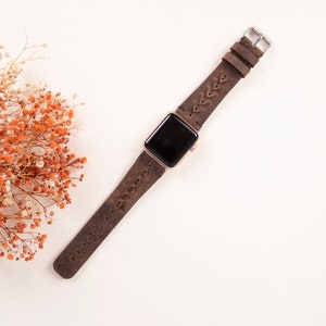Puede incluir: Una correa de reloj de cuero marr&oacute;n con un dise&ntilde;o trenzado. La correa est&aacute; unida a un Apple Watch de oro rosa.