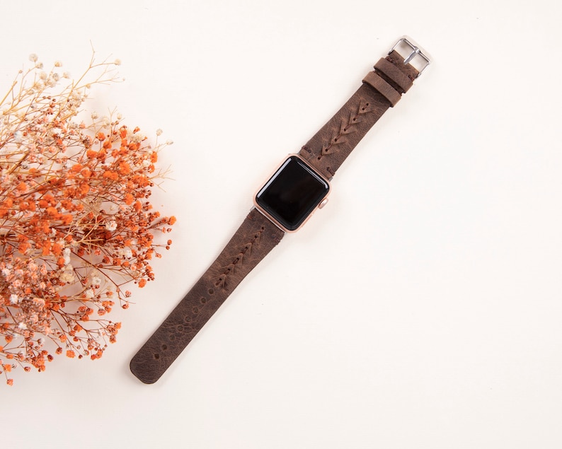 Puede incluir: Una correa de reloj de cuero marr&oacute;n con un dise&ntilde;o trenzado. La correa est&aacute; unida a un Apple Watch de oro rosa.