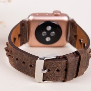 Puede incluir: Una correa de reloj de cuero marr&oacute;n con un Apple Watch de oro rosa. La correa tiene un dise&ntilde;o trenzado y una hebilla plateada.