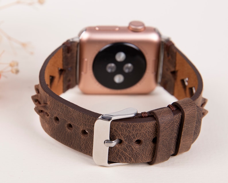Puede incluir: Una correa de reloj de cuero marr&oacute;n con un Apple Watch de oro rosa. La correa tiene un dise&ntilde;o trenzado y una hebilla plateada.