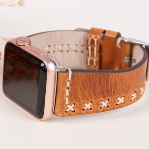May include: A brown leather Apple Watch band with white stitching. The band has a classic look and is compatible with Apple Watch models.