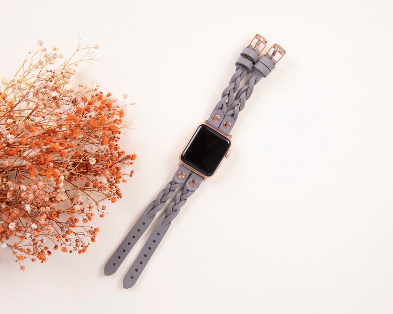 Peut inclure: Un bracelet de montre en cuir tress&eacute; gris avec des d&eacute;tails en or rose. Le bracelet est con&ccedil;u pour une Apple Watch.