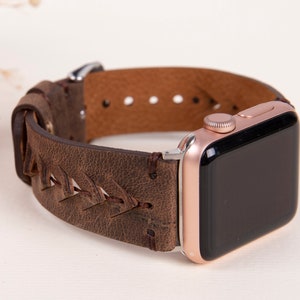 Puede incluir: Una correa de reloj de cuero marr&oacute;n con un dise&ntilde;o trenzado. La correa est&aacute; unida a un Apple Watch de oro rosa.