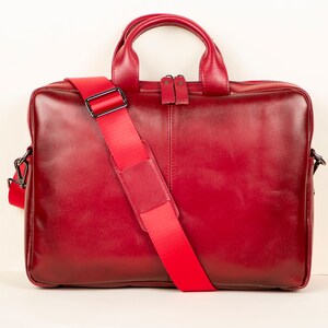 Op de afbeelding: Een rode leren laptoptas met een lange verstelbare schouderband. De tas heeft een bovenste handvat en een ritssluiting.