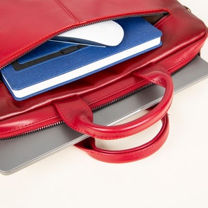 Op de afbeelding: Een rode leren laptoptas met een ritssluiting en een handvat. De tas is open en er zit een laptop, een notitieboekje en een draadloze muis in.