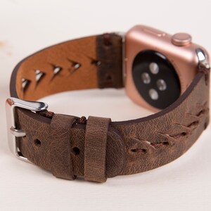 Puede incluir: Una correa de reloj de cuero marr&oacute;n con un dise&ntilde;o trenzado y una hebilla plateada. La correa est&aacute; dise&ntilde;ada para un Apple Watch y tiene una esfera de reloj de oro rosa.