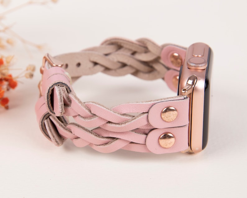 Peut inclure: Un bracelet en cuir tress&eacute; rose avec des accessoires en or rose pour une Apple Watch.