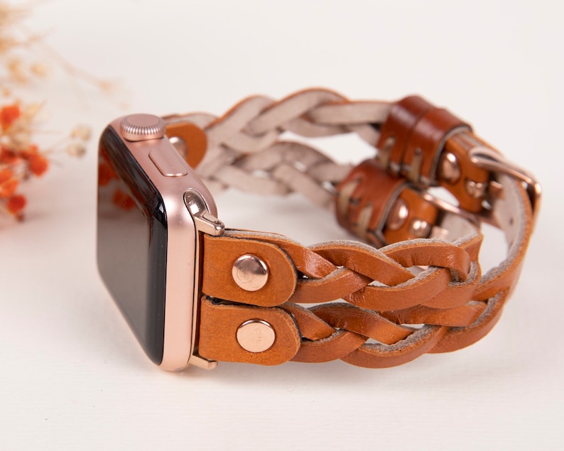 Peut inclure: Un bracelet de montre en cuir tress&eacute; de couleur marron et beige avec des d&eacute;tails en or rose. Le bracelet est con&ccedil;u pour une Apple Watch.