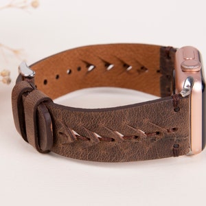 Puede incluir: Una correa de reloj de cuero marr&oacute;n con un dise&ntilde;o trenzado y un Apple Watch de oro rosa.