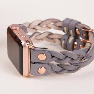 Peut inclure: Un bracelet en cuir tress&eacute; gris avec des d&eacute;tails en or rose pour une Apple Watch.