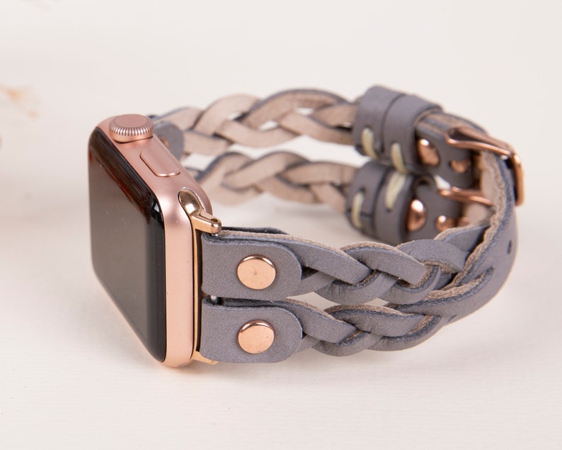 Peut inclure: Un bracelet en cuir tress&eacute; gris avec des d&eacute;tails en or rose pour une Apple Watch.